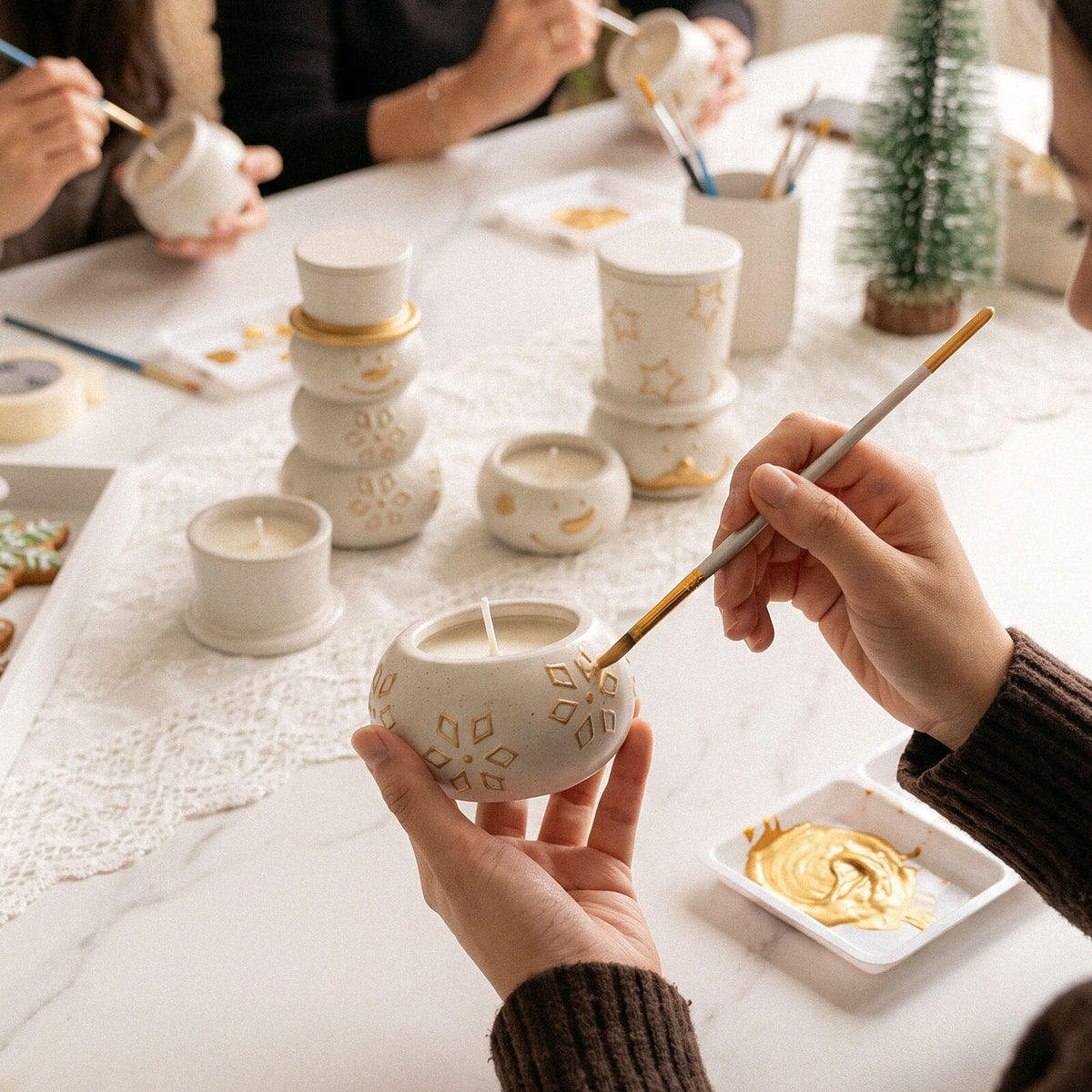 Painting gold details on snowman candle jars at a holiday table
