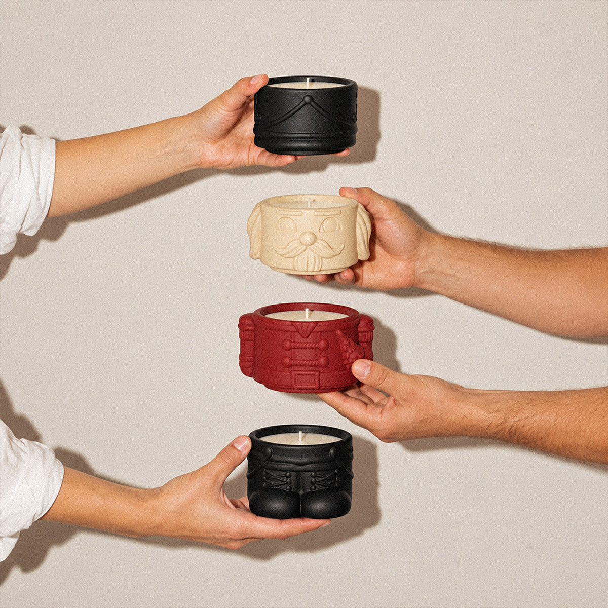 Hands stacking black, cream and red nutcracker candle jar sections