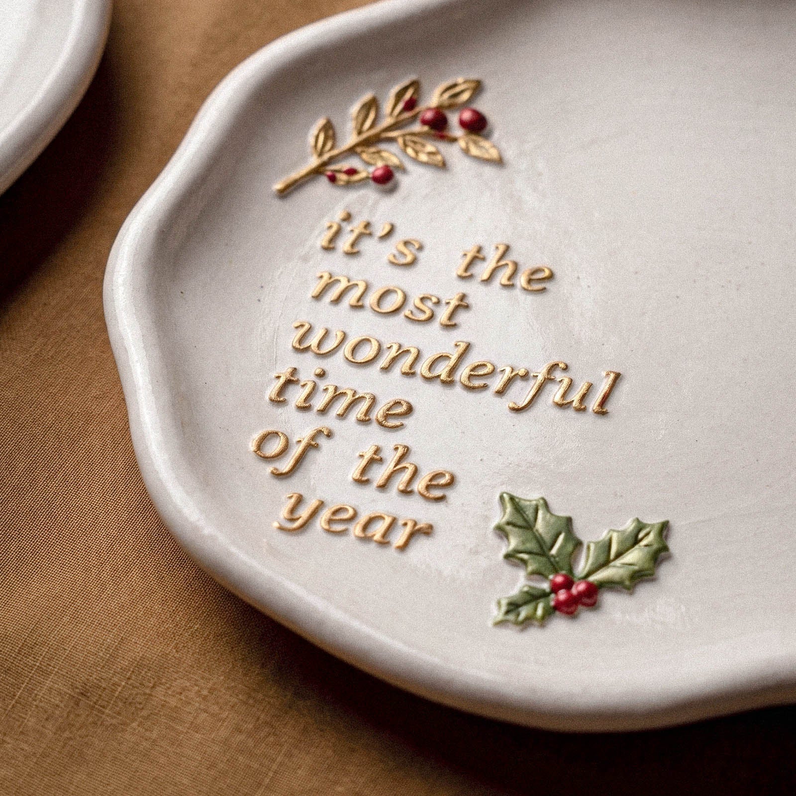 Close-up of a white trinket tray with a gold botanical branch, red berries, and It's the Most Wonderful Time of the Year lettering with a green holly accent.