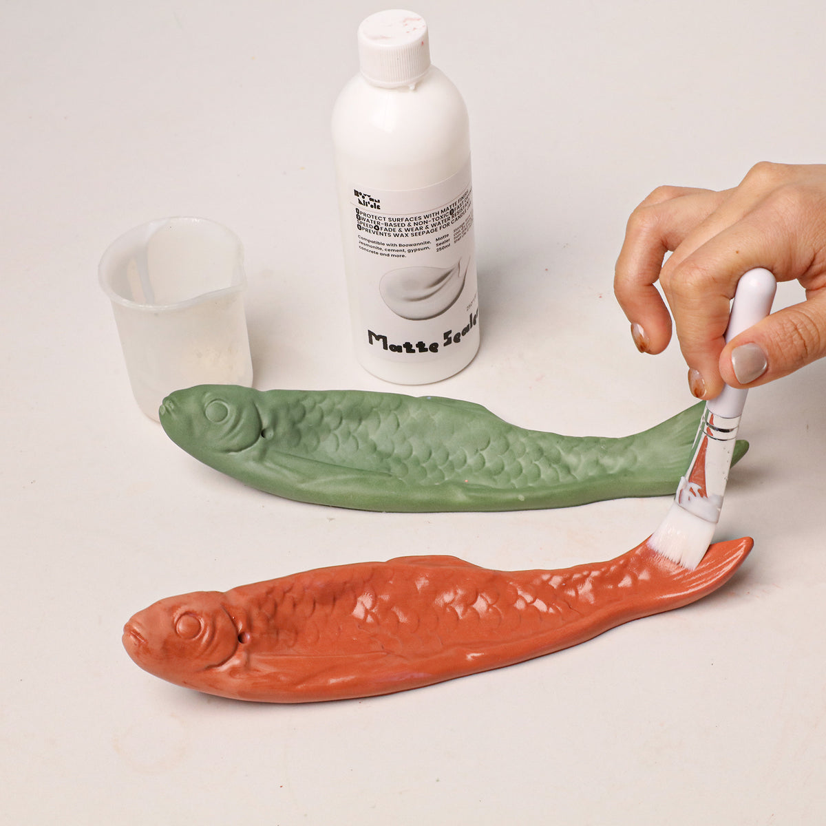 Applying matte sealer to red and green fish incense holders
