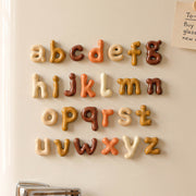 Rounded lowercase alphabet letters arranged on a wall in cream, ochre, orange and brown