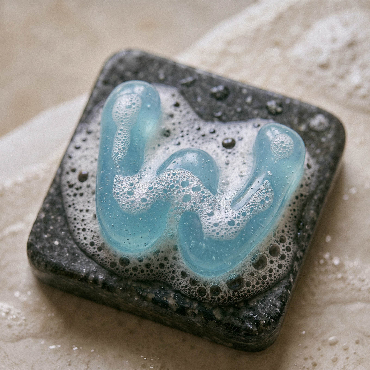 Blue lowercase letter w soap resting on a dark soap dish with bubbles