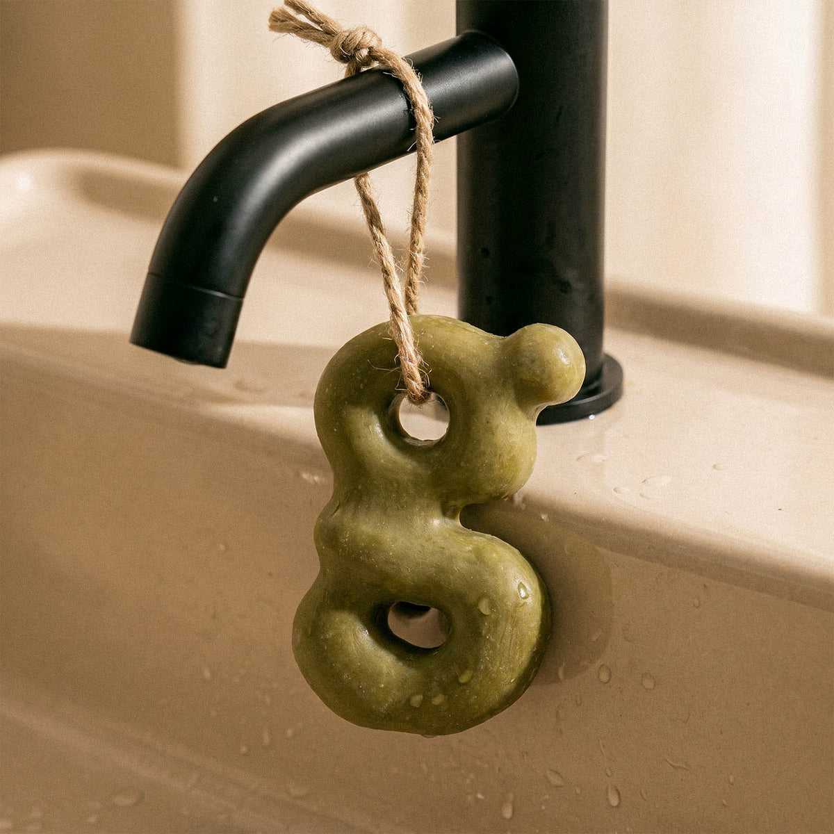Green lowercase letter g soap hanging by a cord from a black faucet
