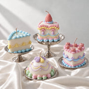 Four pastel buttercream-style cake candles with piped borders and fruit details on glass cake stands