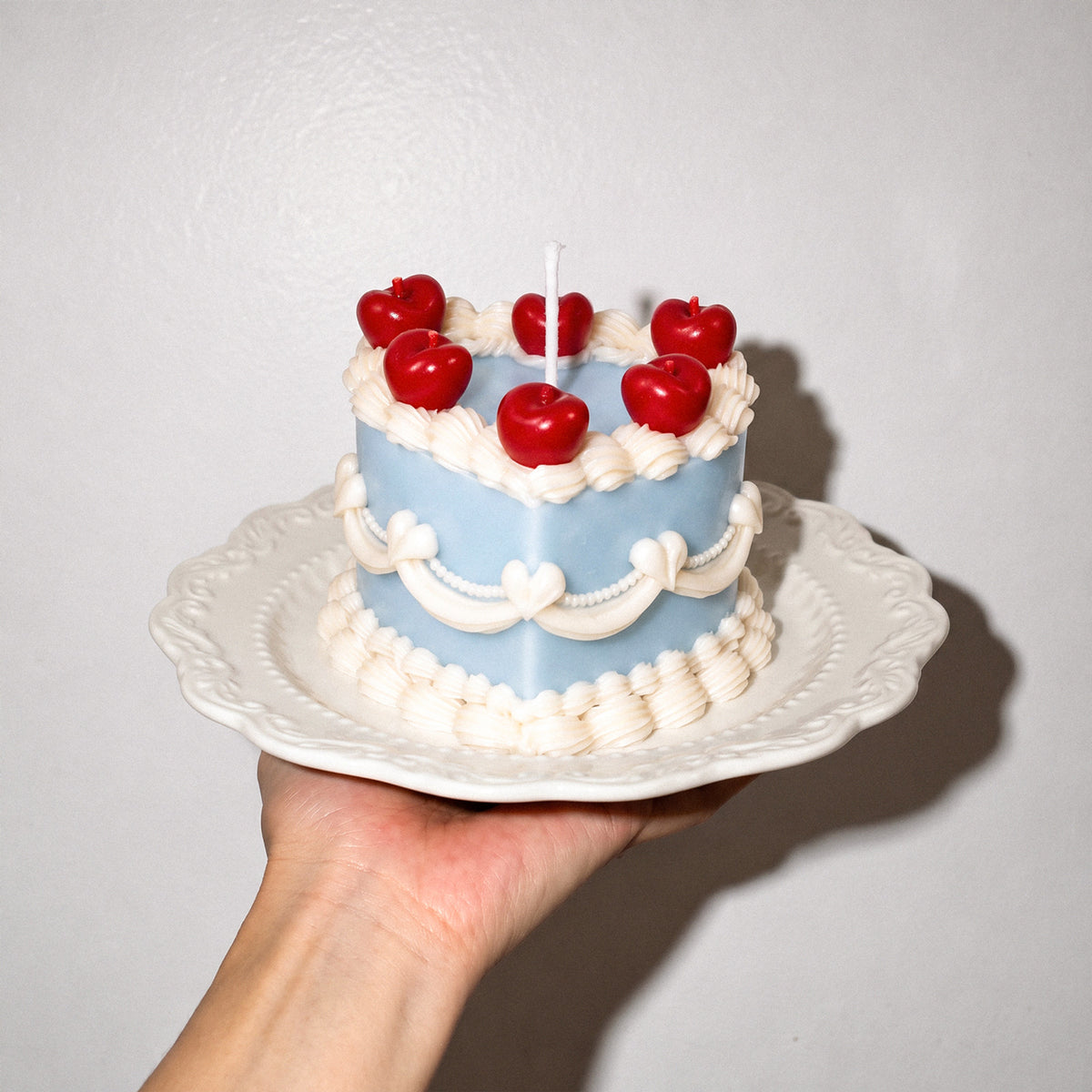 Hand holding a round cake candle with red cherry-shaped details