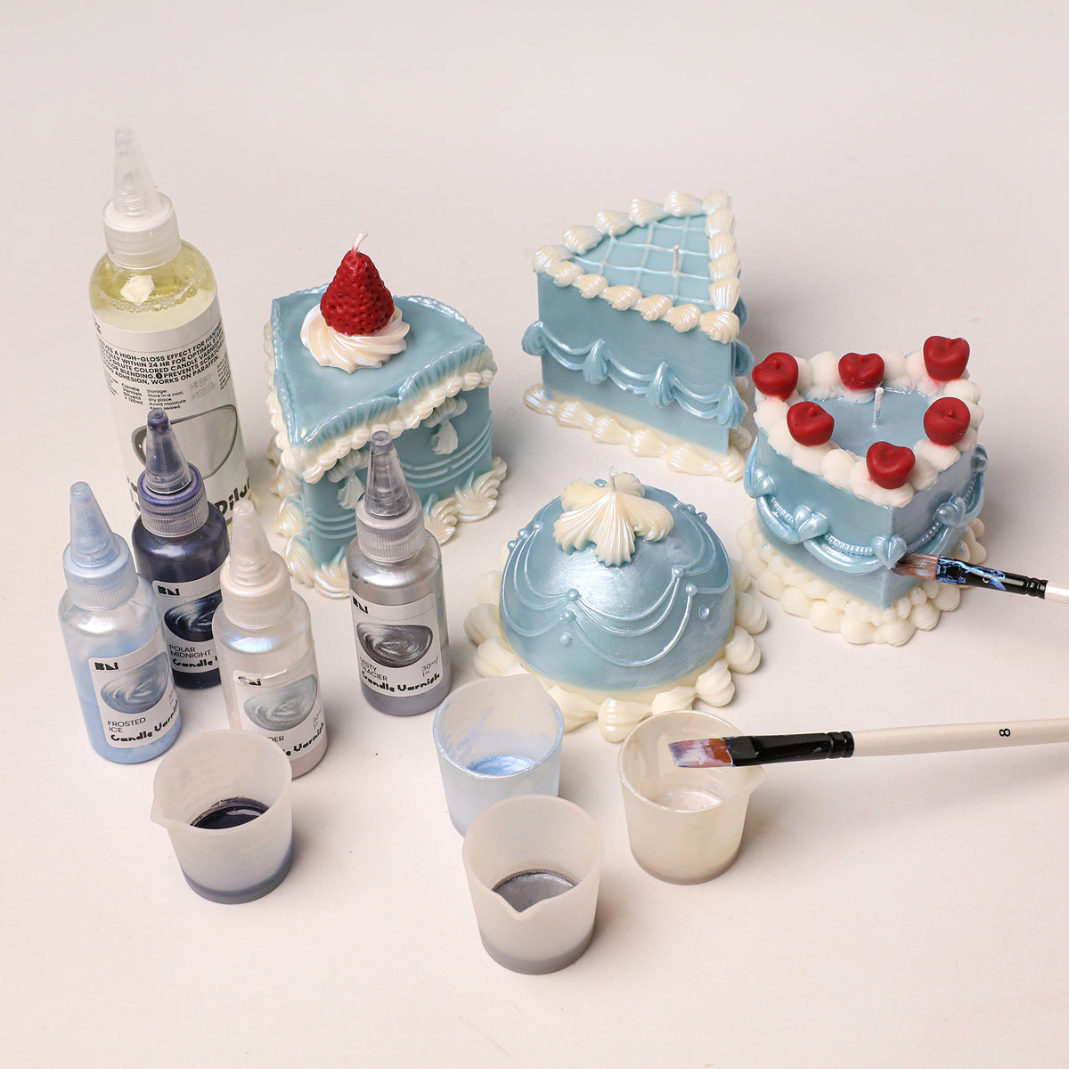 Cake candle decorating setup with candle varnishes, brushes and measuring cups