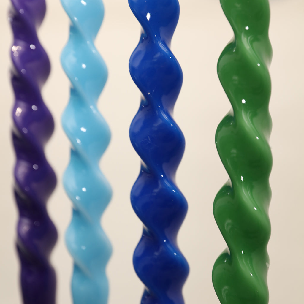 A close-up view of the four Spiral Taper Candle-Boowan Nicole in green, green, blue and purple