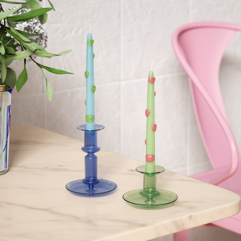 One blue taper candle with green heart accents and one green taper candle with red heart accents on a tabletop candlestick-Boowan Nicole