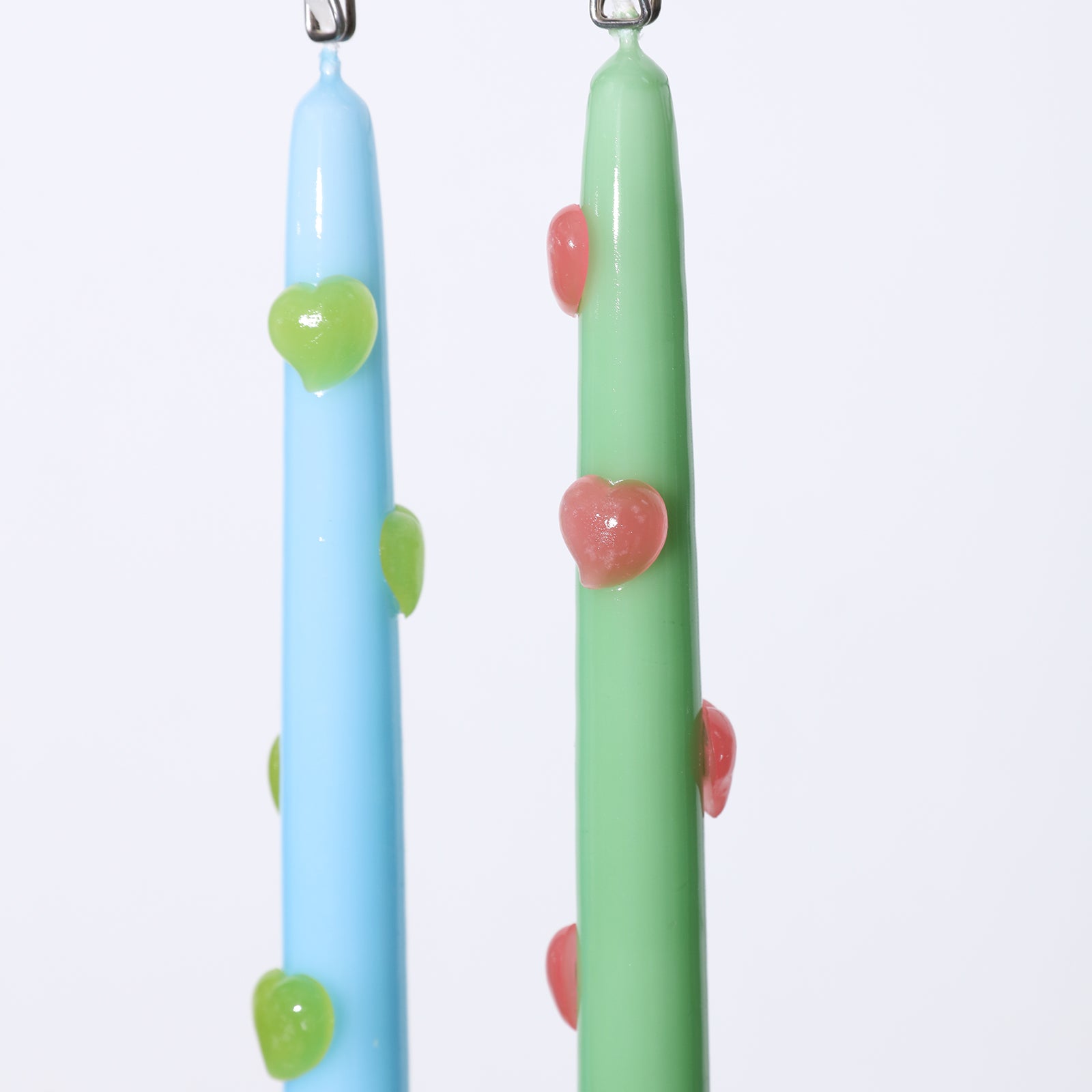 One blue taper candle with green heart accents and one green taper candle with red heart accents hanging from a clip - Boowan Nicole