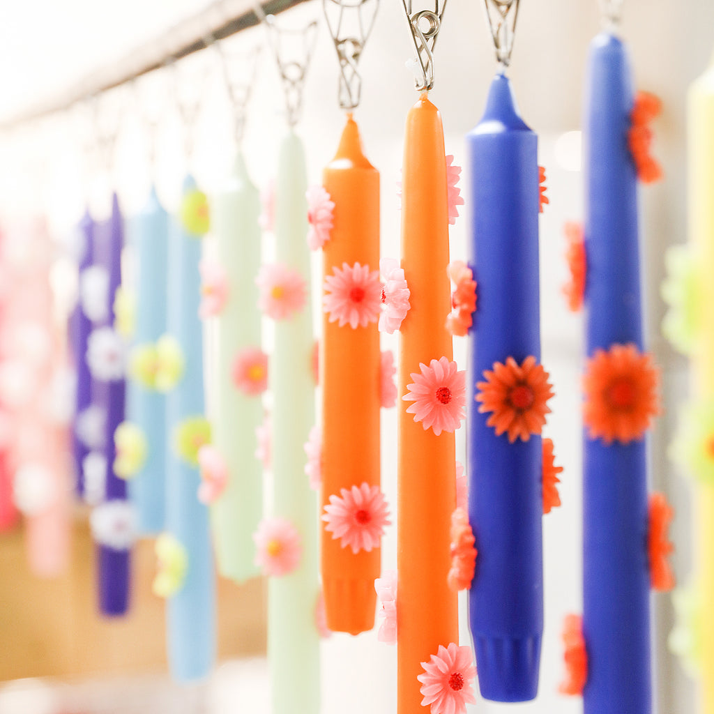 Daisy taper candles in various colors hanging from a clip on a shelf-Boowan Nicole