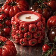 Red tomato-cluster candle jar with a wooden wick, surrounded by tomatoes