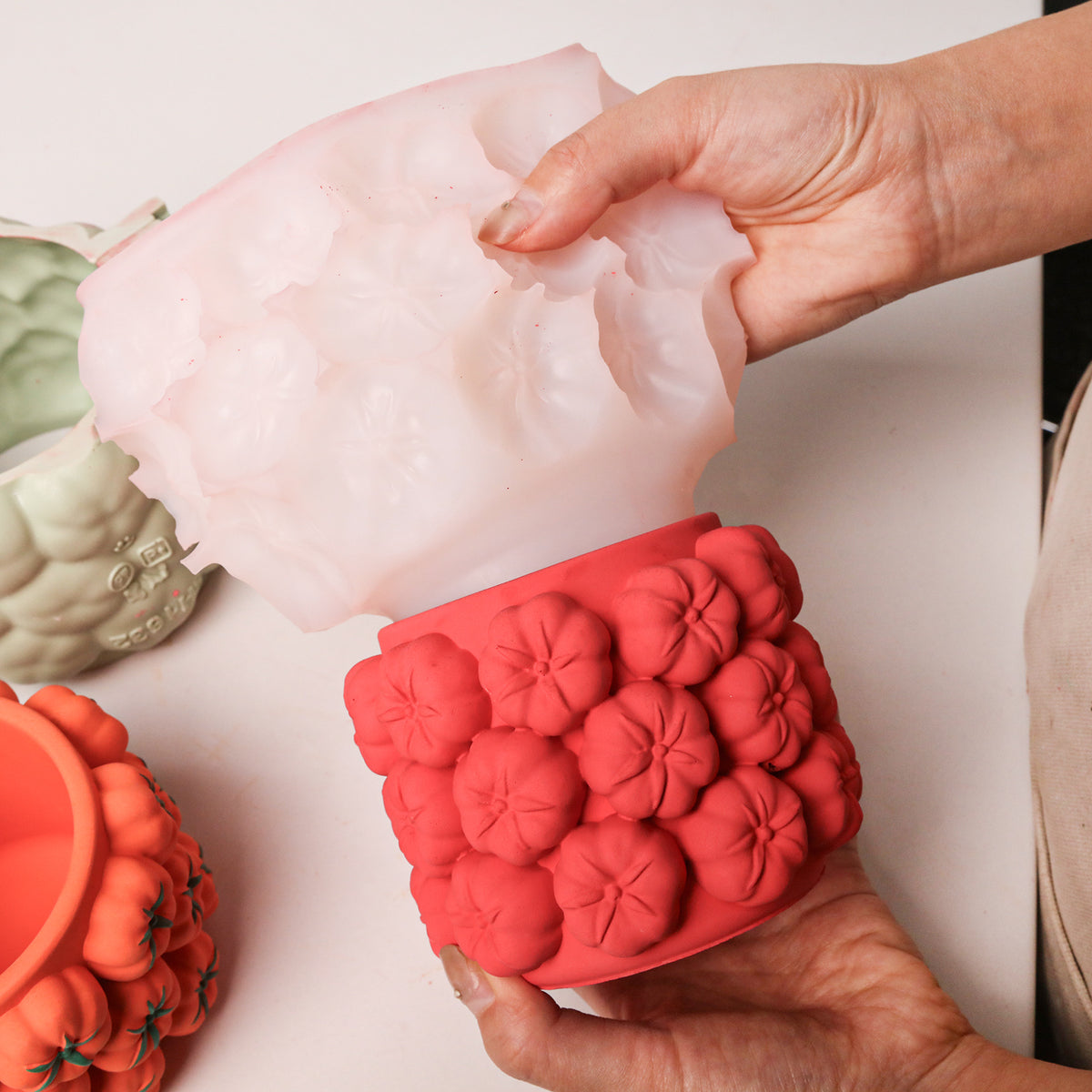 Peeling the silicone mold away from a red tomato-cluster jar