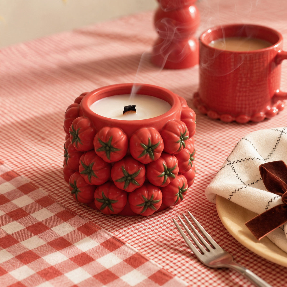 Red tomato-cluster candle jar styled with tableware on a gingham tablecloth