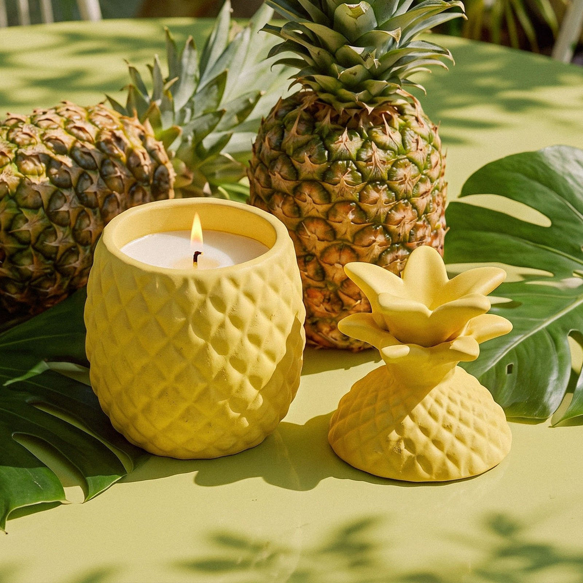Lit pineapple candle jar beside fresh pineapples