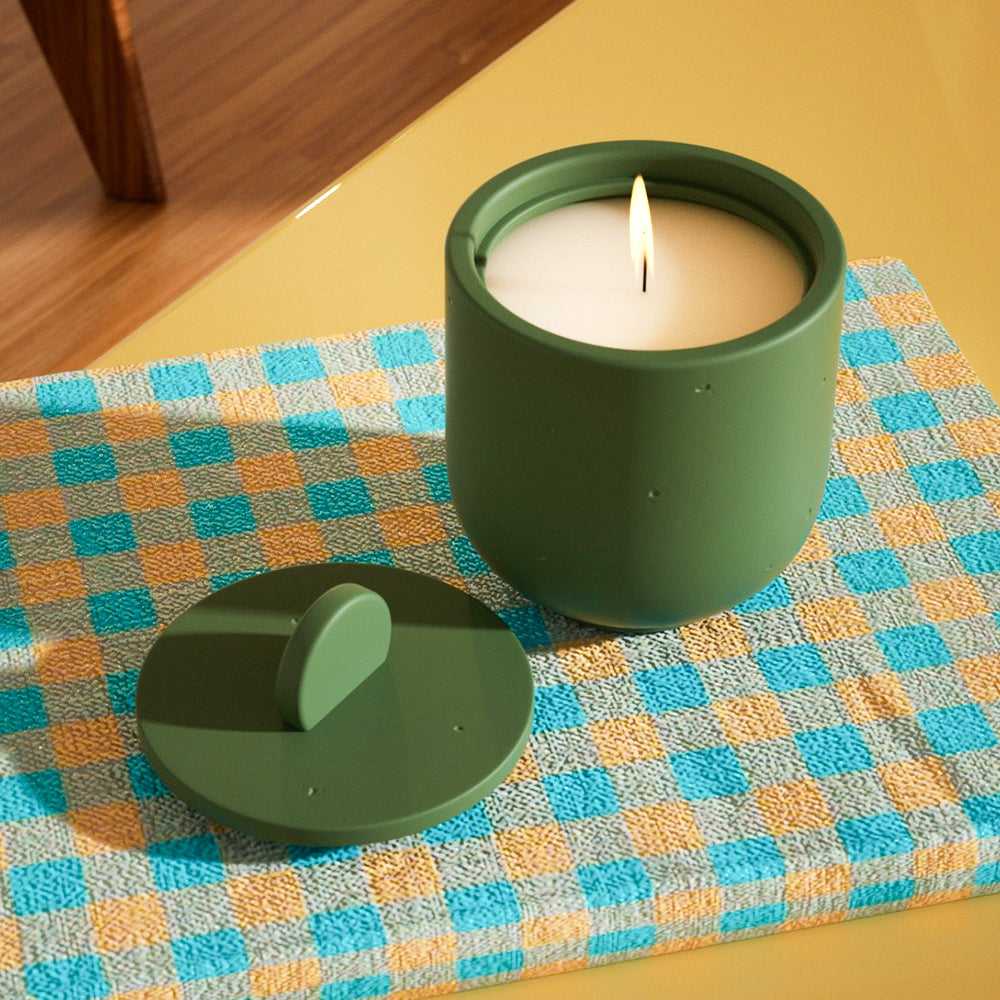 Deep green candle jar aglow, candle burning; handle-equipped lid placed nearby, showcasing Boowannicole's allure.