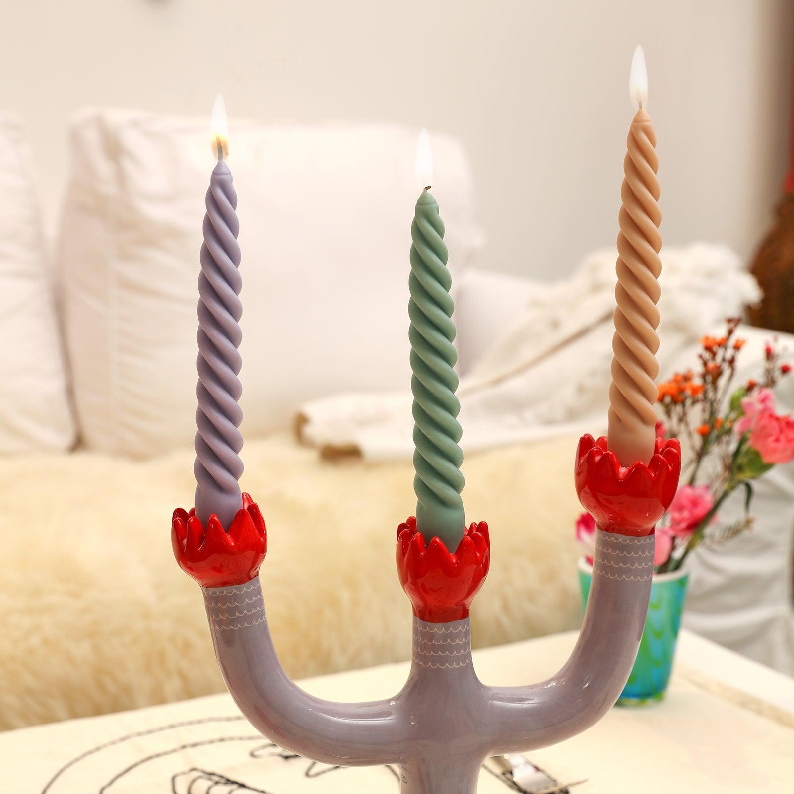 Three elegantly lit taper candles adorn the candle holder, casting a warm glow against the background of a cozy sofa.