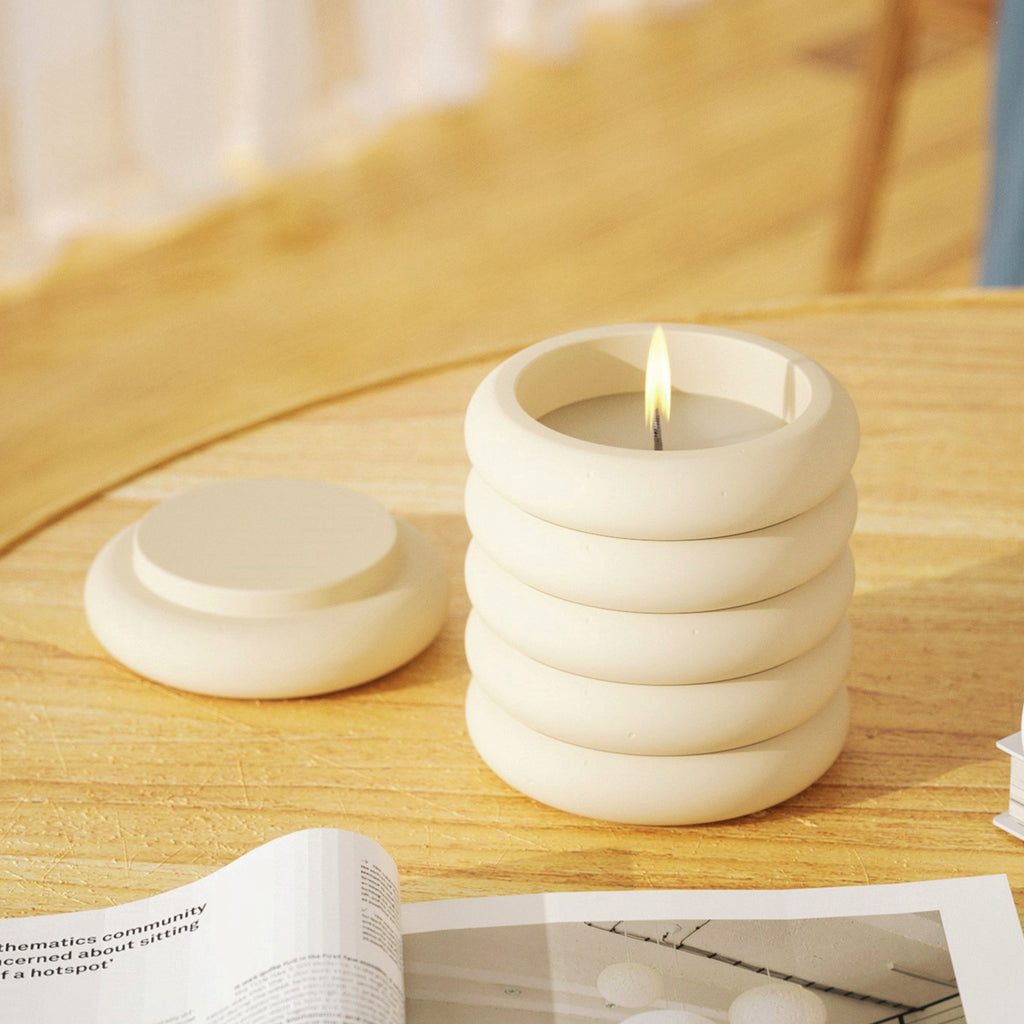 On the table, a candle burns in a Boowannicole jar, accompanied by a book. A serene moment, where unique design harmonizes with a cozy atmosphere.
