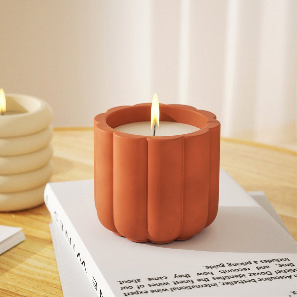 A candle gracefully burns inside a candle jar, resting atop a stack of artfully arranged books, showcasing candle jars in distinct and vibrant hues