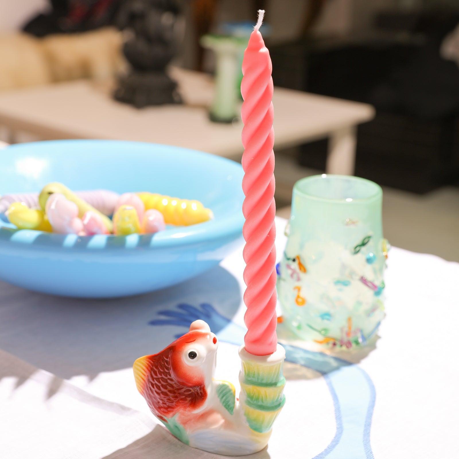 Sunlight bathes a pink candle, crafted with Boowannicole's silicone molds, gracefully placed on a candle holder, adorning the tabletop.