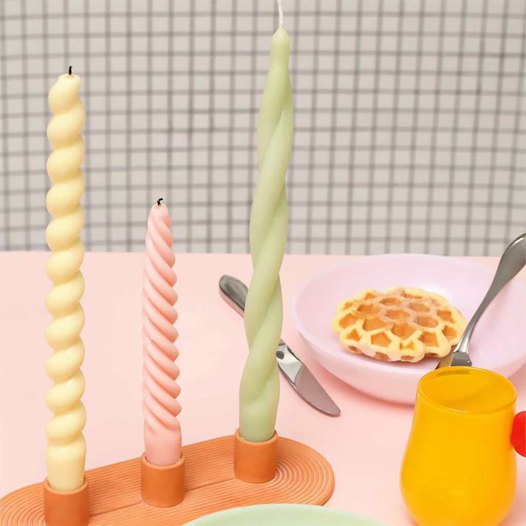 Three taper candles, meticulously crafted with Boowannicole silicone molds, stand elegantly on a candle holder, which in turn graces a dining table.