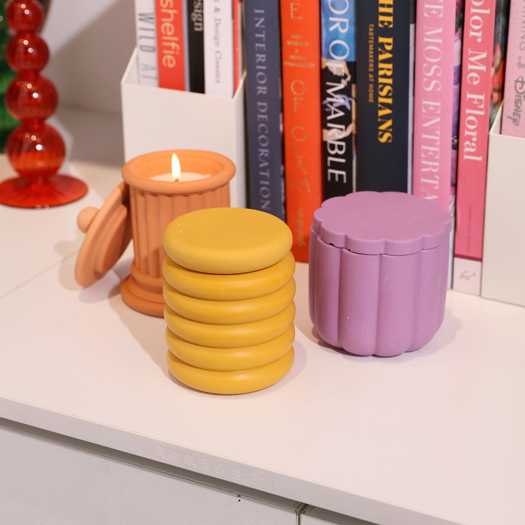 Next to the bookshelf, three distinctively designed boowannicole candle jars are displayed, with one being lit and casting a warm glow