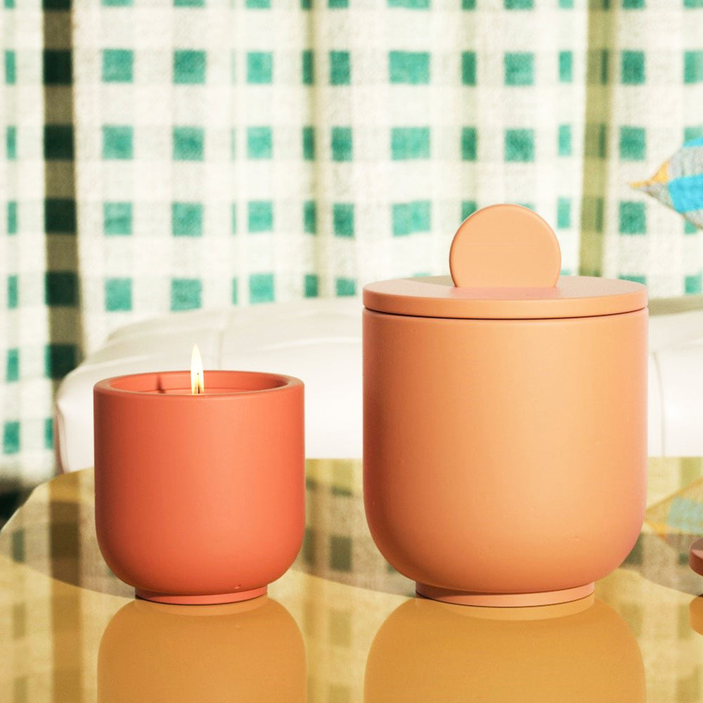 Displaying two Boowannicole orange candle jars on a tabletop—one large, one small. The smaller jar is gracefully lit, adding a warm touch.